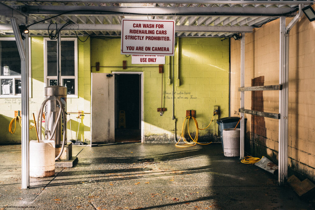  Empty car wash station with a sign prohibiting ride-hailing cars, sunlight casting long shadows.