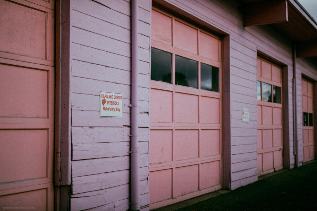 Pink garage doors with a weathered sign reading 'Capilano Custom Interiors Upholstery Shop.