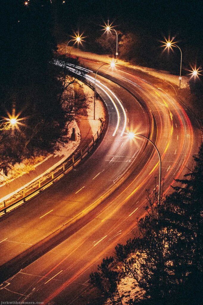 Long exposure of a curved road at night with vehicle light trails and streetlights