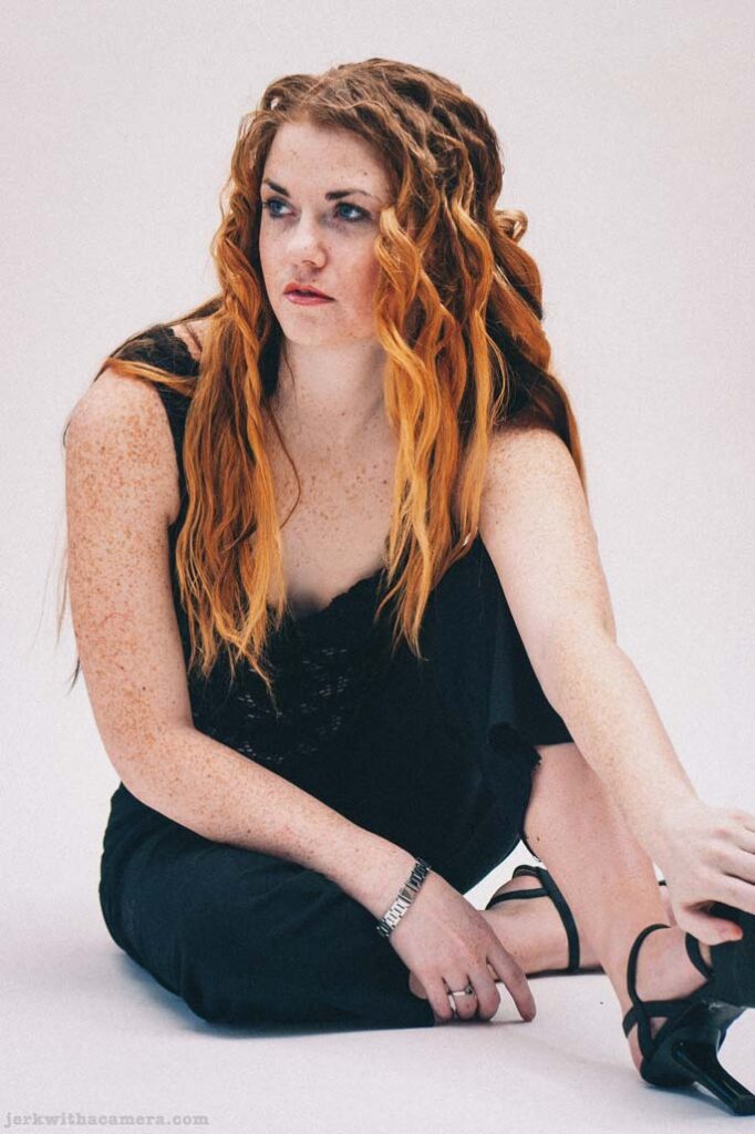 Sommers seated on the studio floor wearing a dark dress and black heels