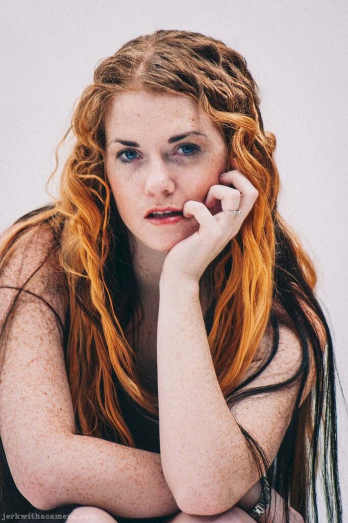 Close portrait of Sommers resting her face on her hand against a white studio background