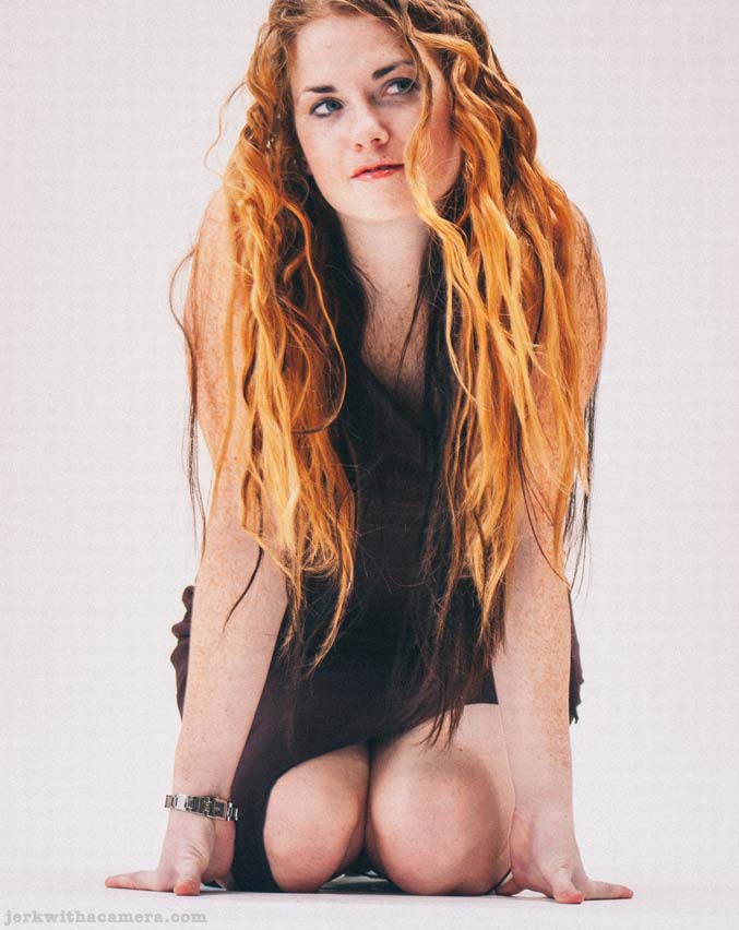Sommers kneeling on the studio floor with long red hair against a white background