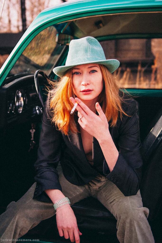 Twilla Coates seated in a Volkswagen Beetle looking toward the camera with a cigarette in hand
