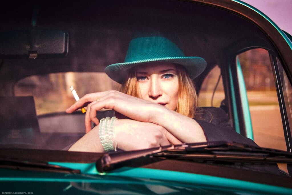 Twilla Coates leaning on the steering wheel of a green Volkswagen Beetle holding a cigarette