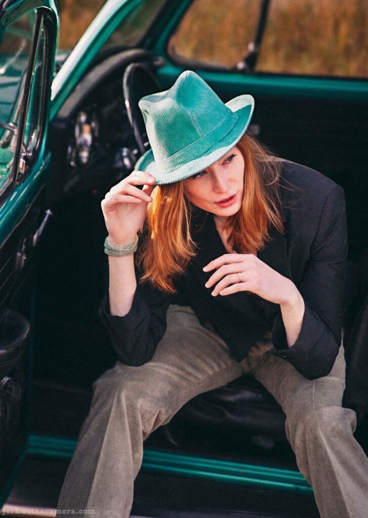 Twilla Coates sitting in the doorway of a green Volkswagen Beetle wearing a teal hat and black jacket