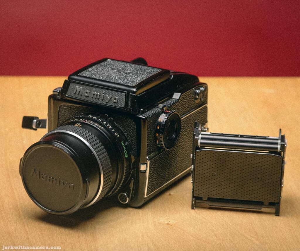 Mamiya medium format camera and detached film back photographed on wooden surface