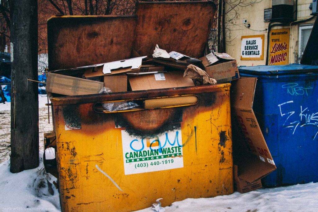 Yellow dumpster filled with cardboard boxes in a snowy alley
