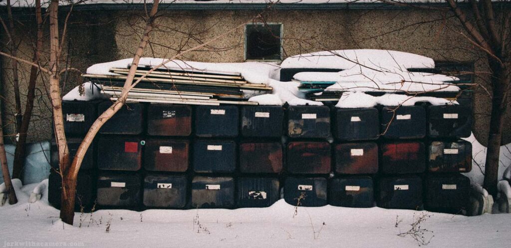 Stacked black plastic containers covered in snow beside a building