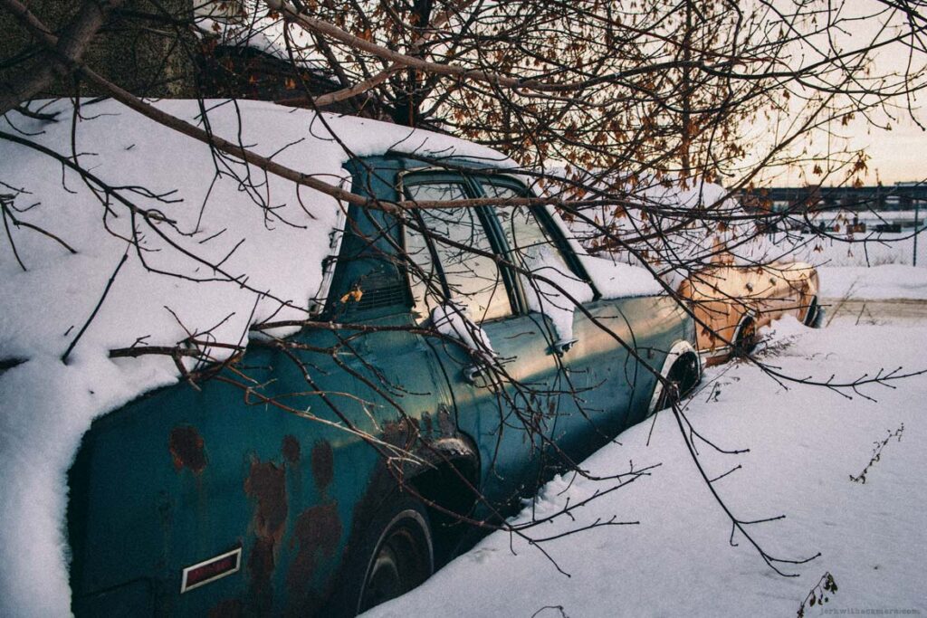 Snow-covered vintage car partially buried beside tree branches