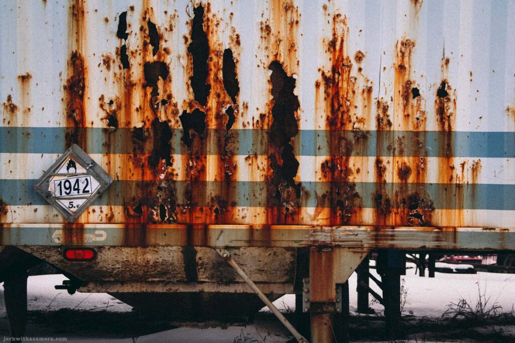 Rusted trailer side with peeling metal and hazard placard