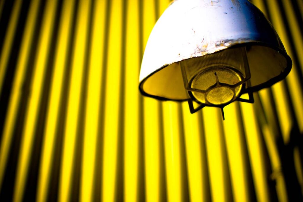 ndustrial light fixture against a vibrant yellow corrugated metal wall.