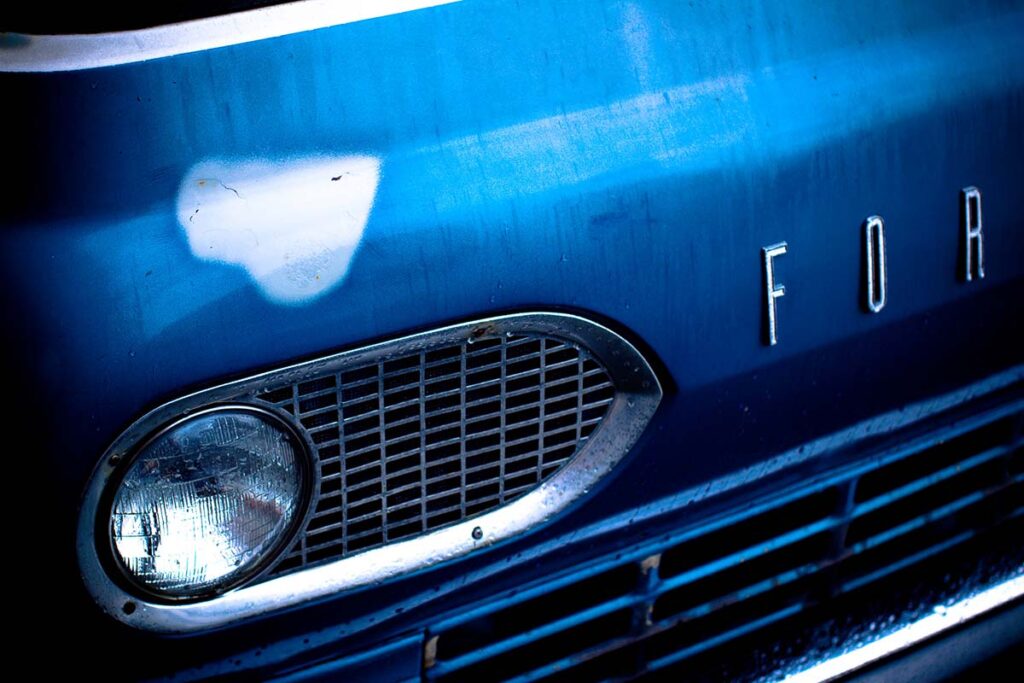 Close-up of a vintage blue Ford truck grille and headlight.