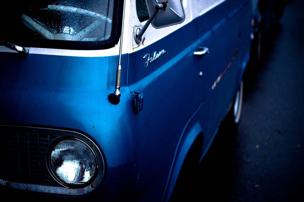 Close-up of a vintage blue Ford truck grille and headlight.