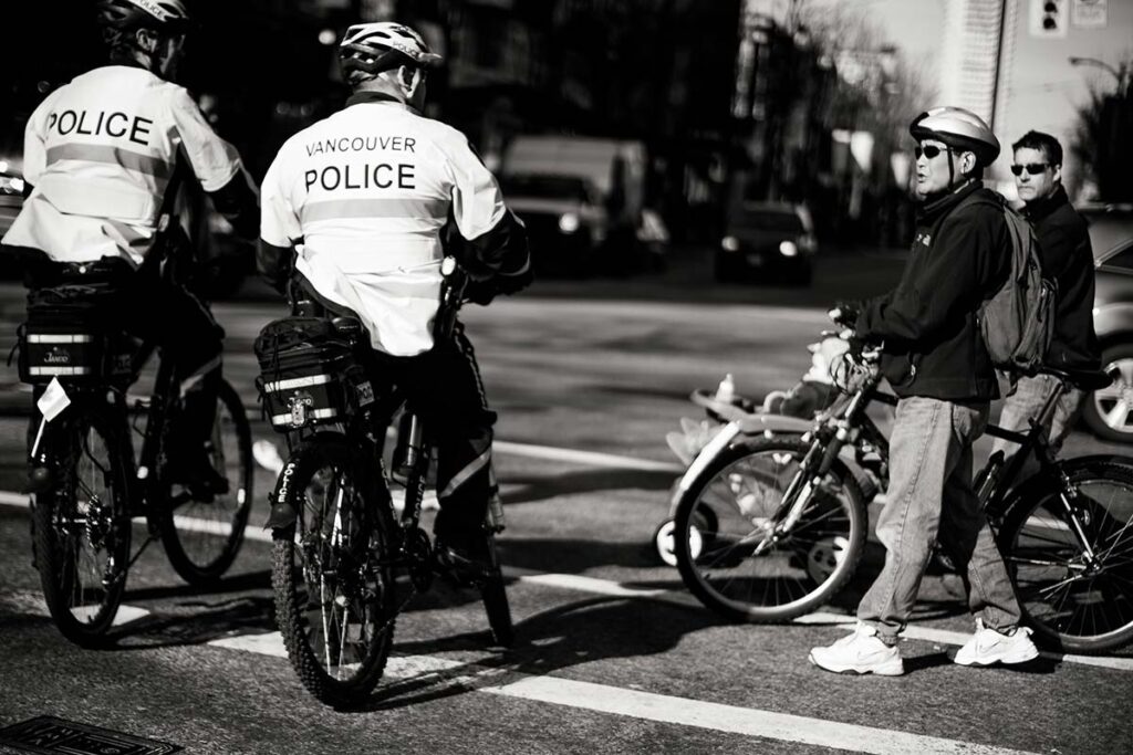 Two Vancouver police officers on bicycles alongside cyclists stopped at an intersection in black and white.