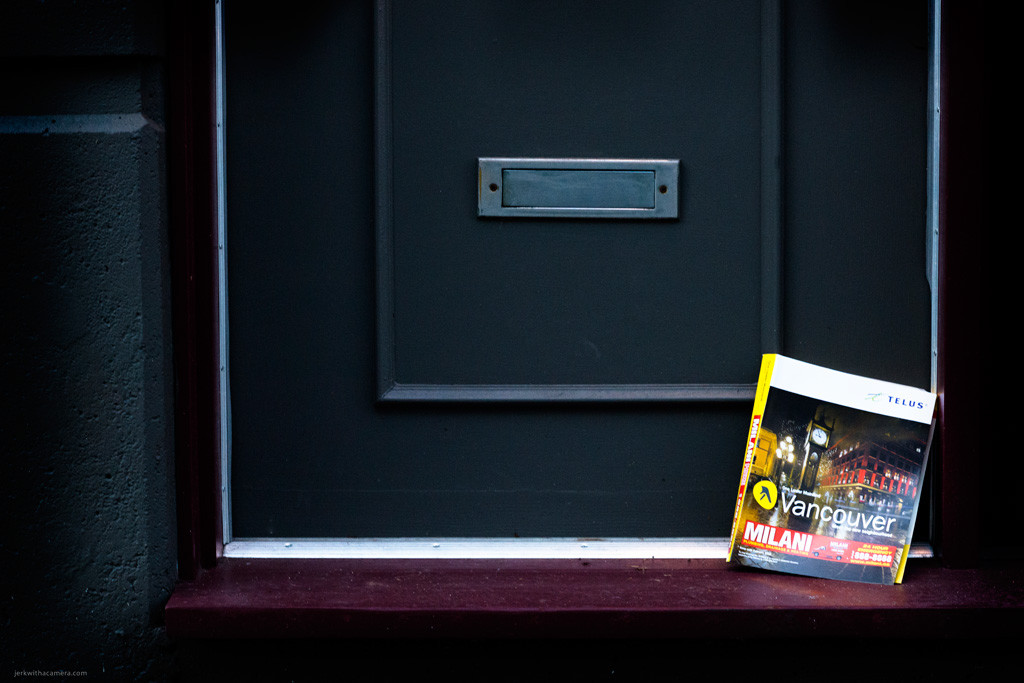 Magazine leaning against a dark door beneath a mail slot.