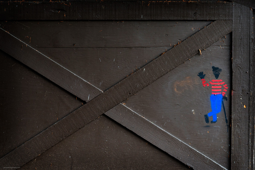 Wooden gate with diagonal braces and a small stencil figure wearing a striped shirt and blue pants.