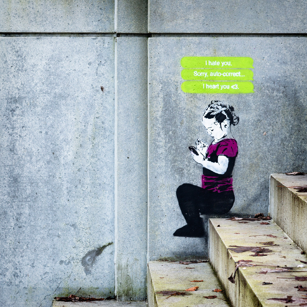 Stencil of a child with text message bubbles on a concrete wall.