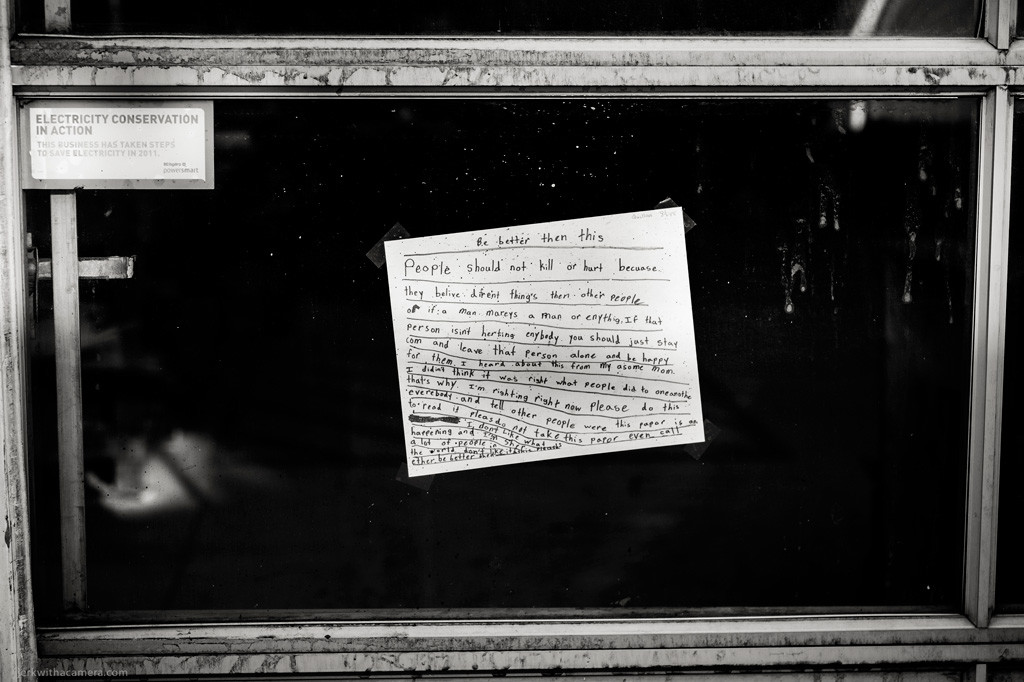 Window with a handwritten note taped to the glass and an electricity conservation sign in the corner.