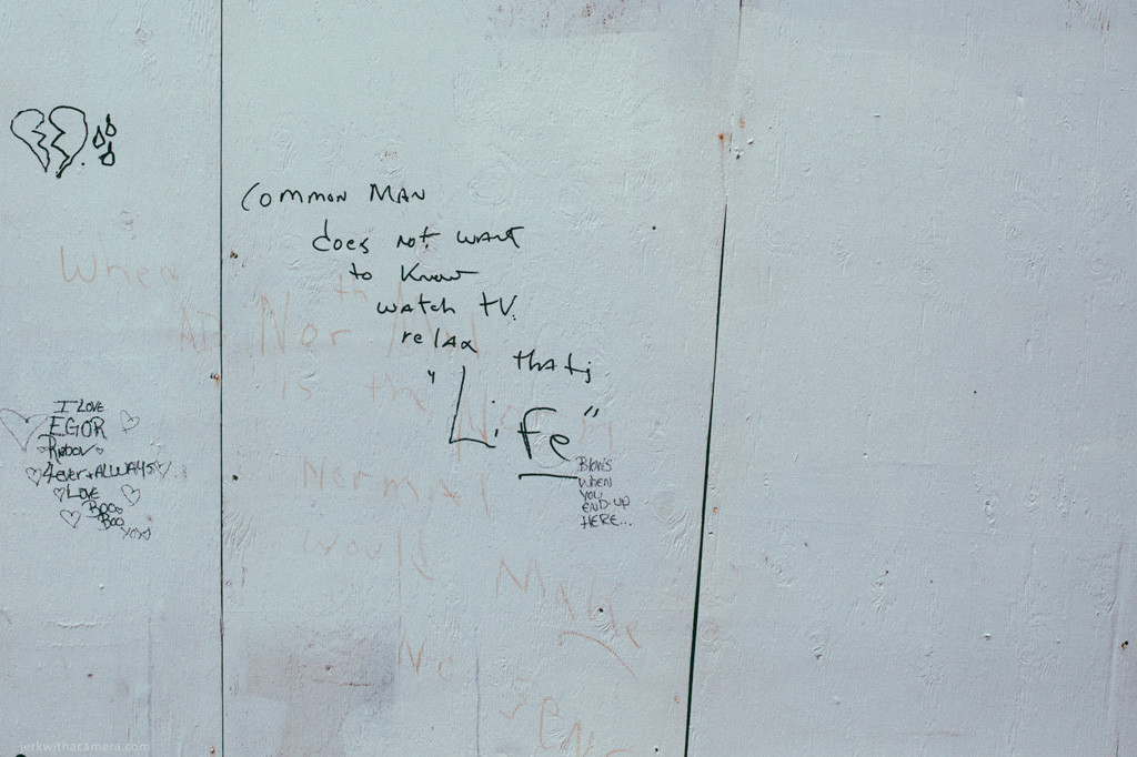 White painted plywood wall with handwritten graffiti, drawings, and text including the word Life written near the center.