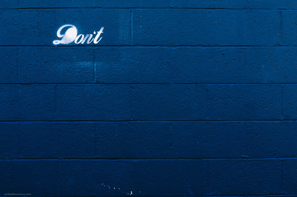 Blue cinder block wall with the word Dont painted in white script near the top.