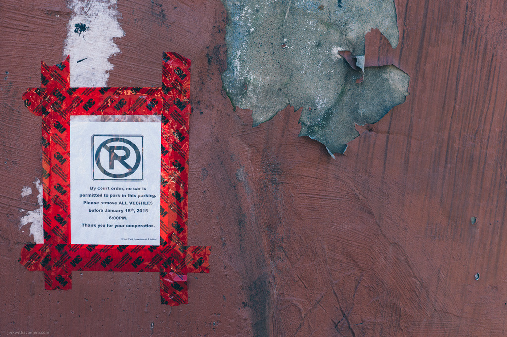 Printed parking notice taped to a plywood wall with red tape beside peeling material.