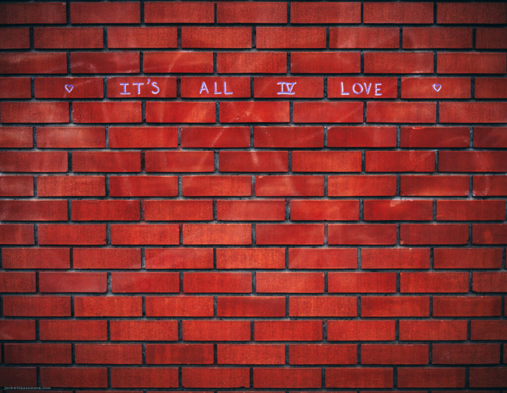 Brick wall with the text "It's All IV Love" written in pink chalk.