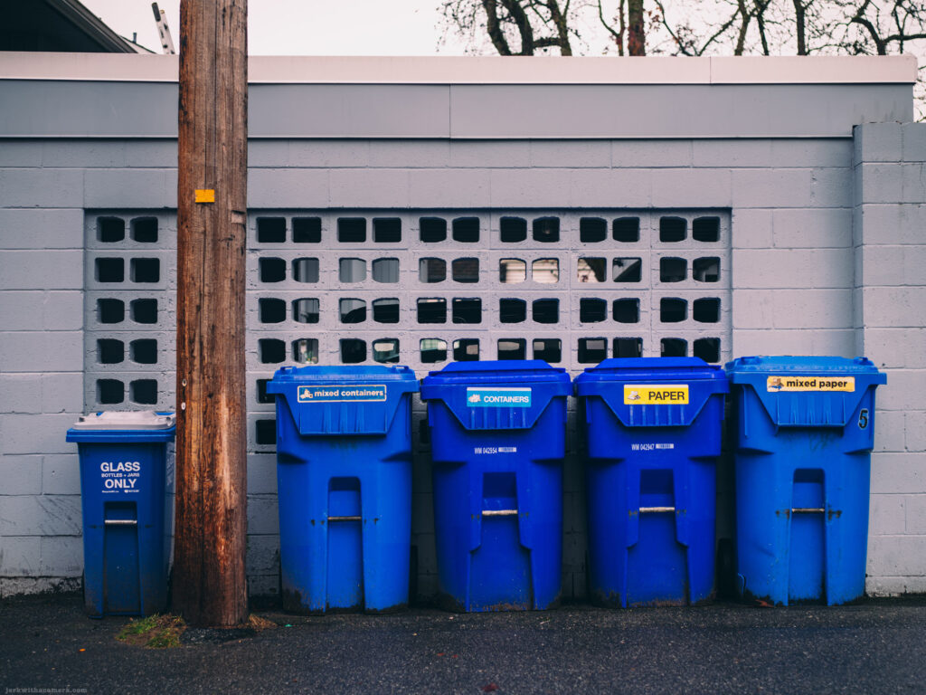 A row of blue recycling bins against a white concrete wall with a wooden utility pole to the left.