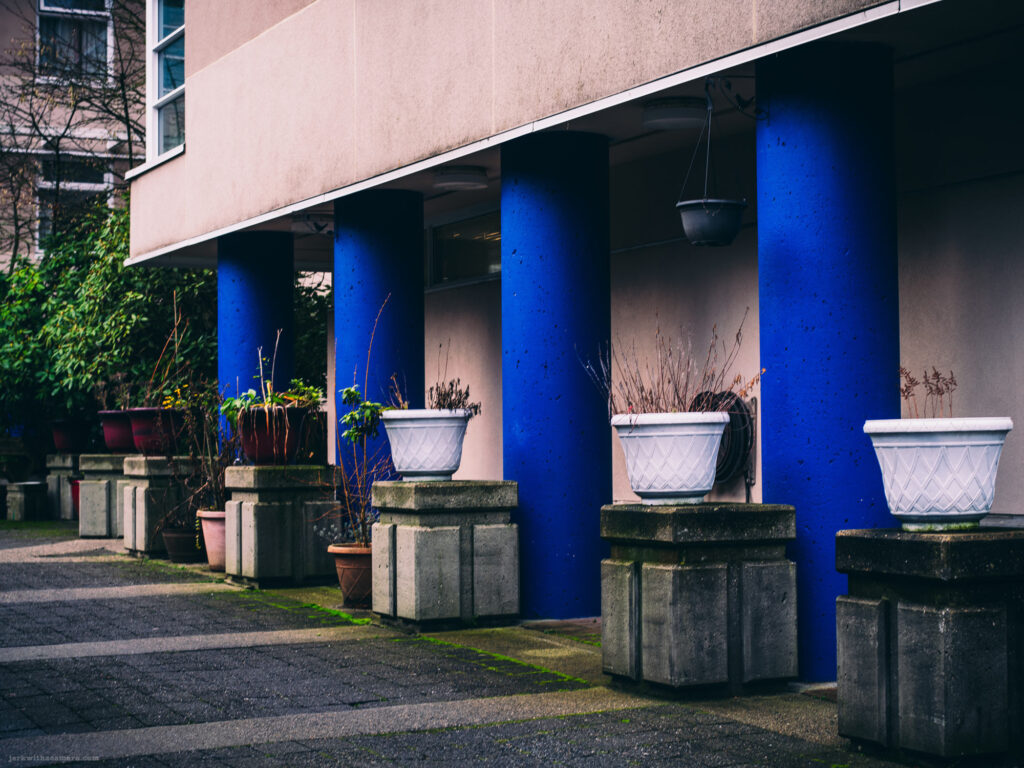 Blue-painted columns with flower pots arranged on concrete blocks in front of a building.