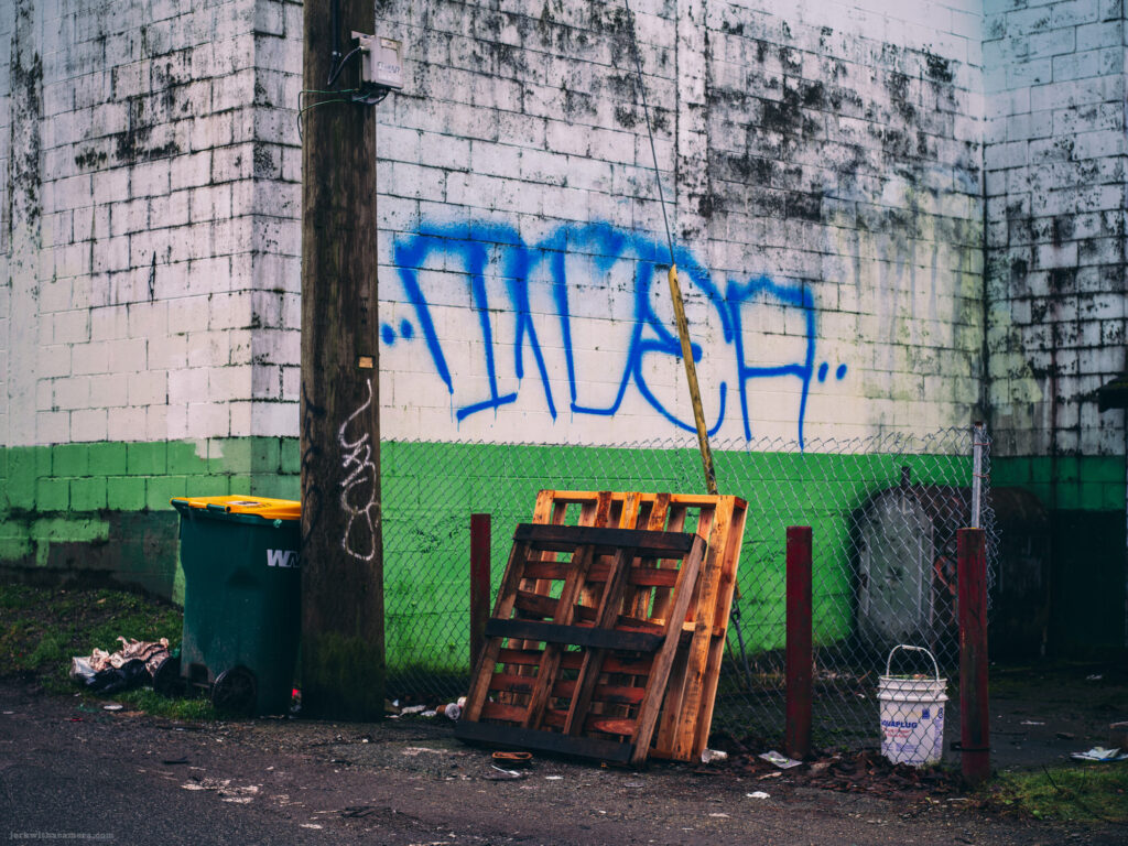 An alleyway scene with graffiti, a wooden pallet, and a green and white wall.