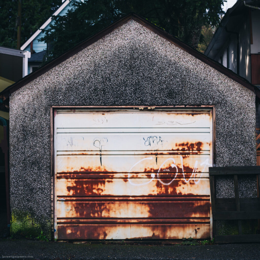 A rusty garage door with graffiti and textured walls.