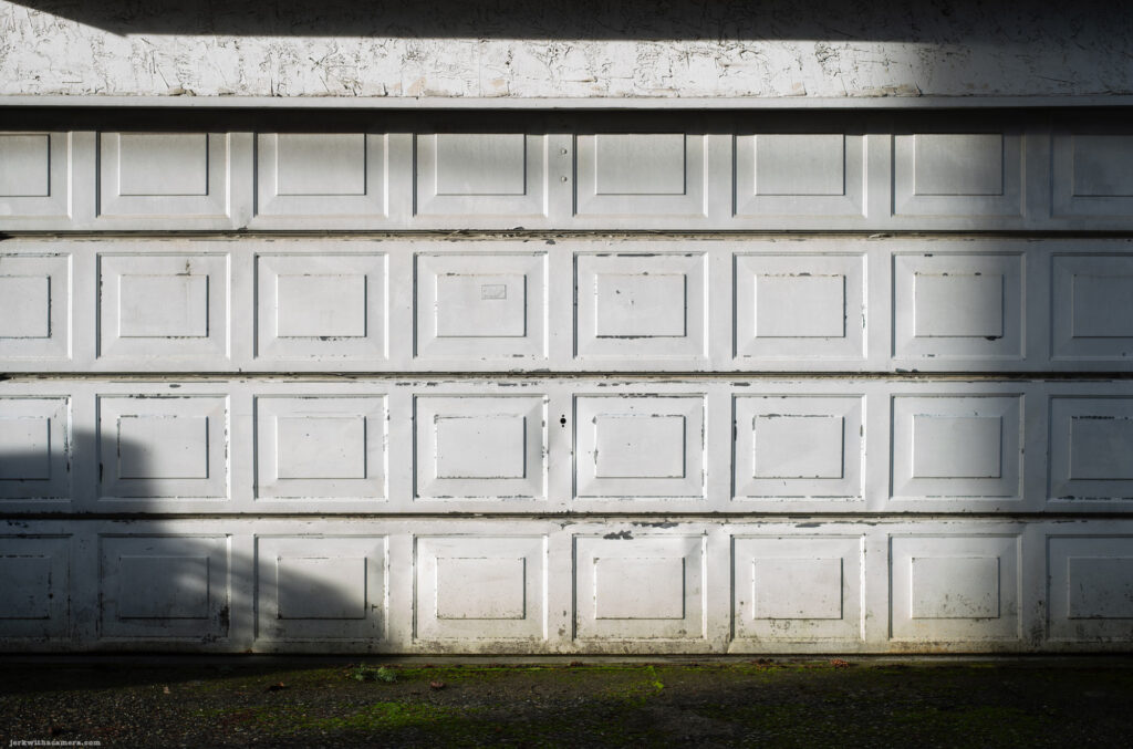 A white garage door with peeling paint, highlighted by afternoon shadows.