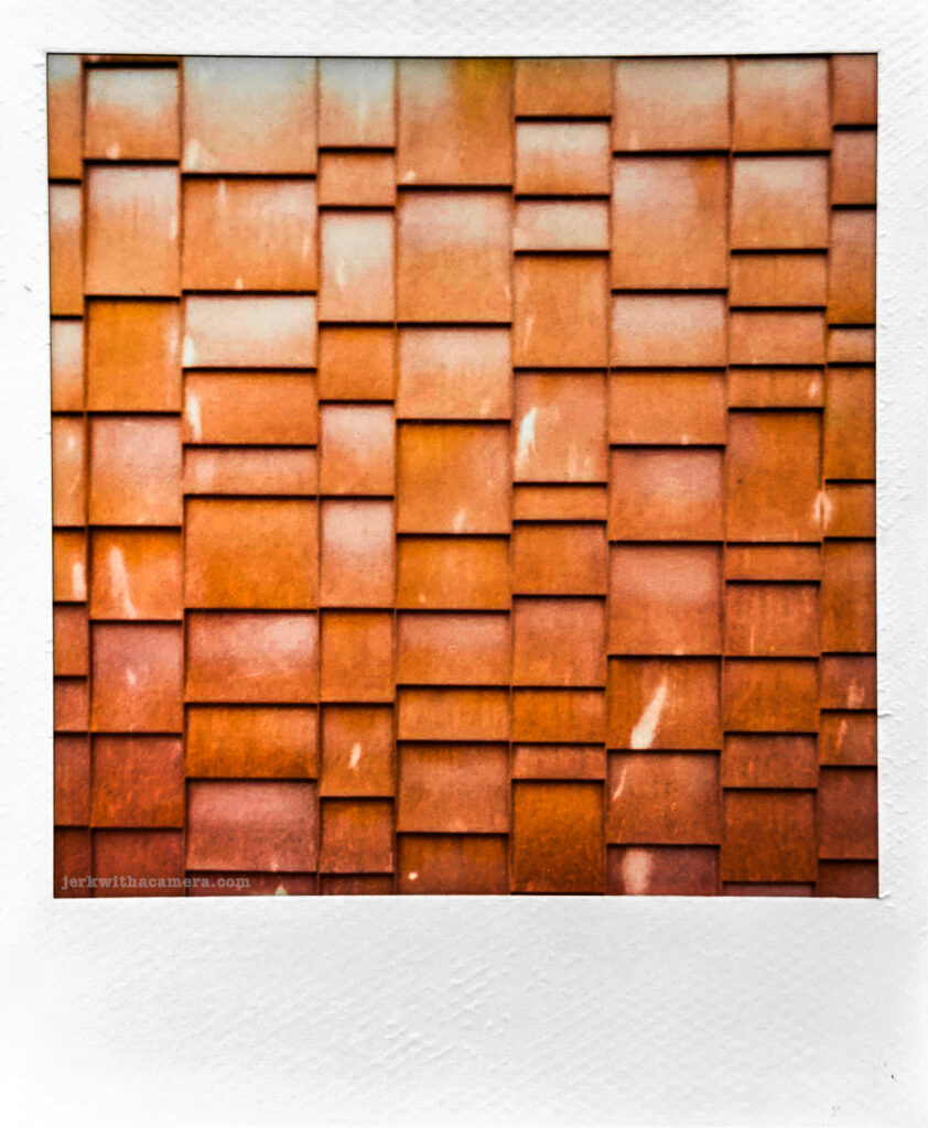 Polaroid photo of overlapping orange cedar shingles on a building exterior
