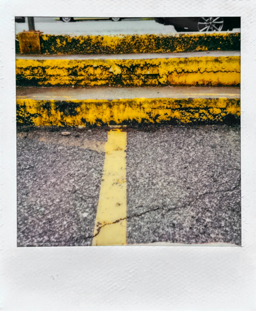 Polaroid photo of weathered yellow-painted concrete steps with a parking lot line