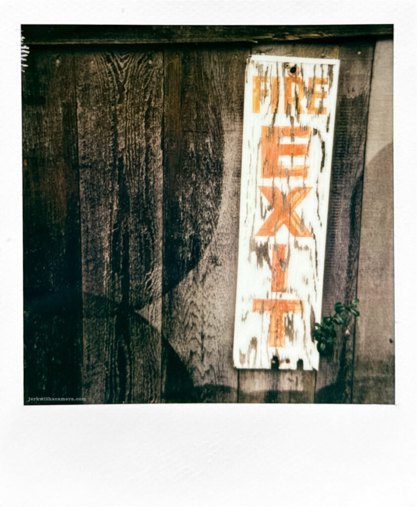 Polaroid photo of a weathered "Fire Exit" sign on a wooden wall