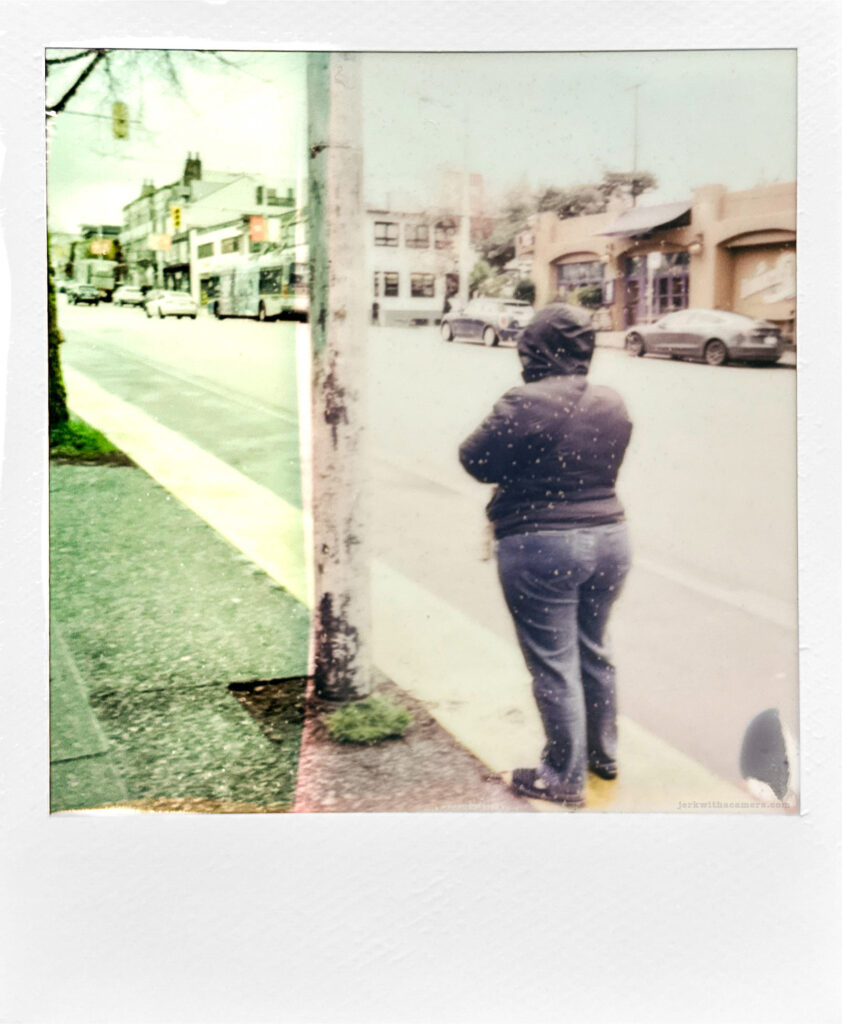 Polaroid photo of a person standing on the sidewalk with motion blur and double exposure.