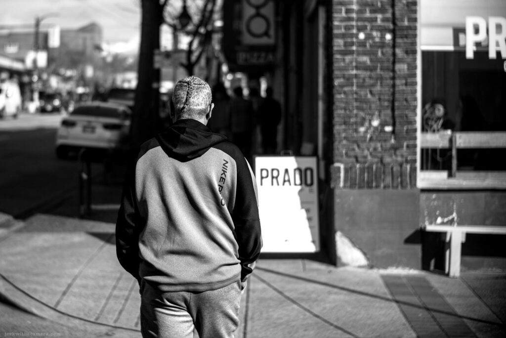 Man in Nike tracksuit walking toward a Prado Cafe sign on Commercial Drive