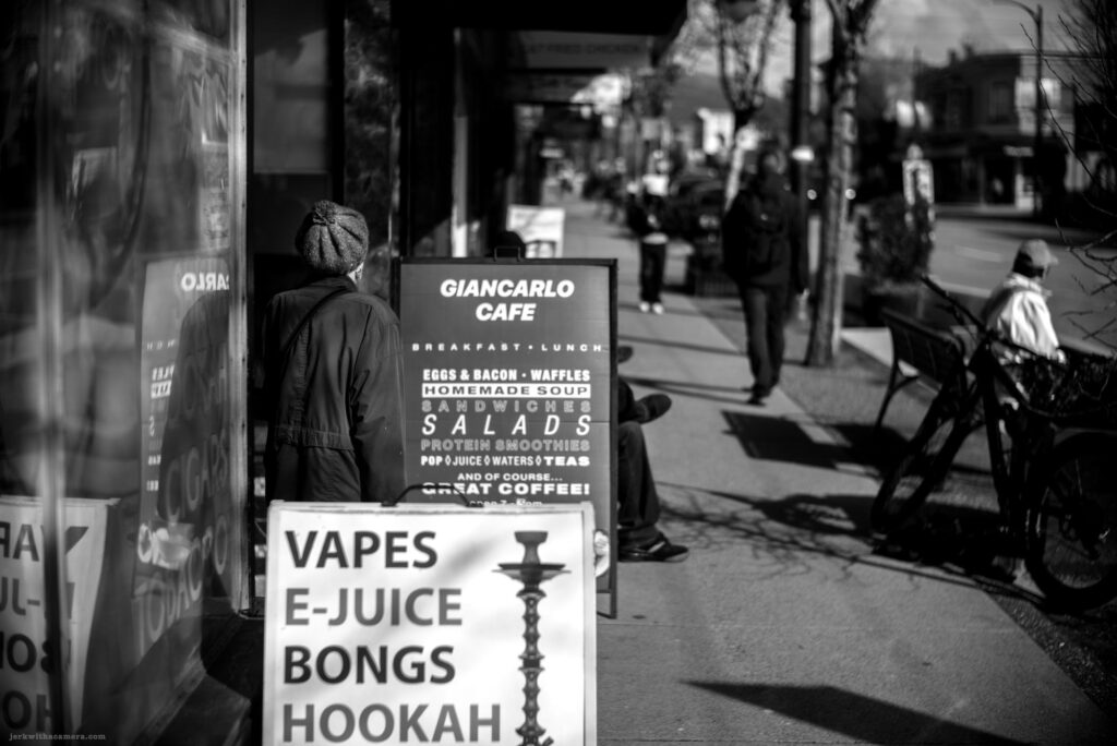 Person standing next to a vape shop sign near Giancarlo Cafe on Commercial Drive