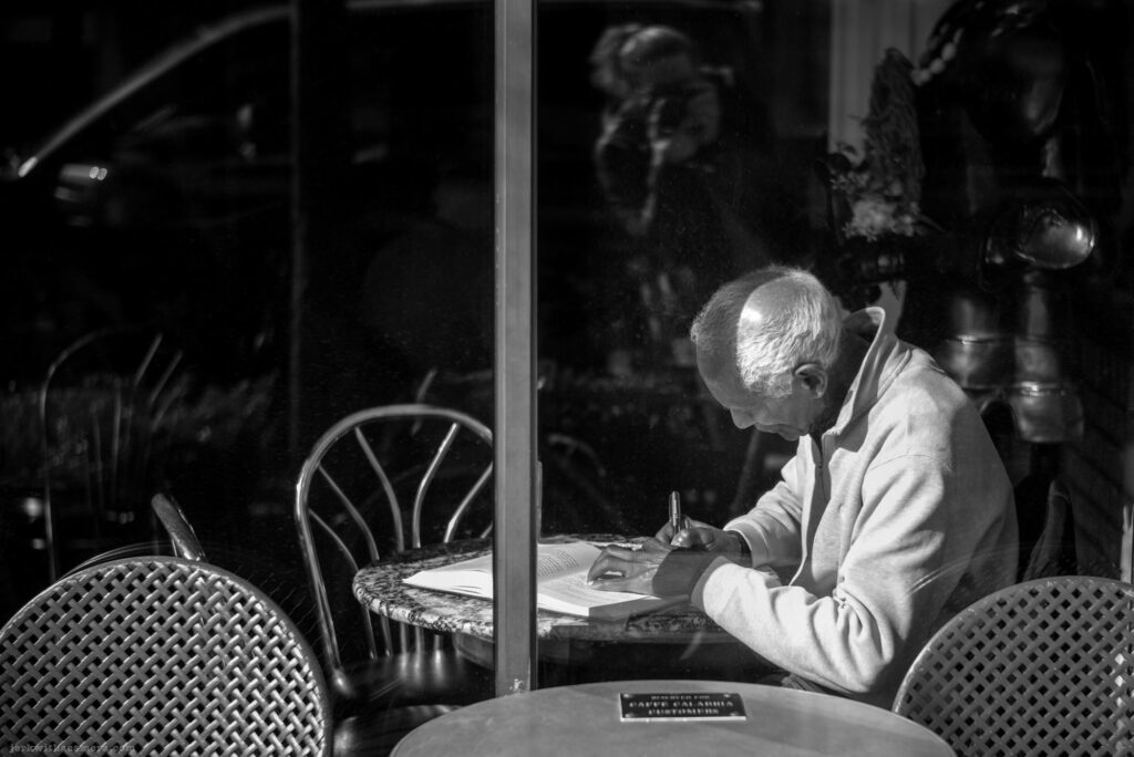 Older man writing in a book at a cafe table indoors