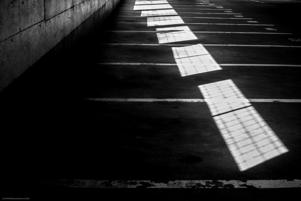 Diagonal light and shadow patterns stretch across empty parking spaces in a garage