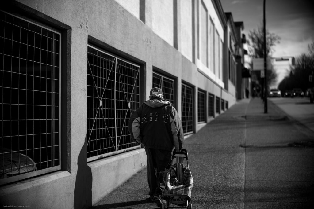 Person pulling a cart past barred windows on the side of a building