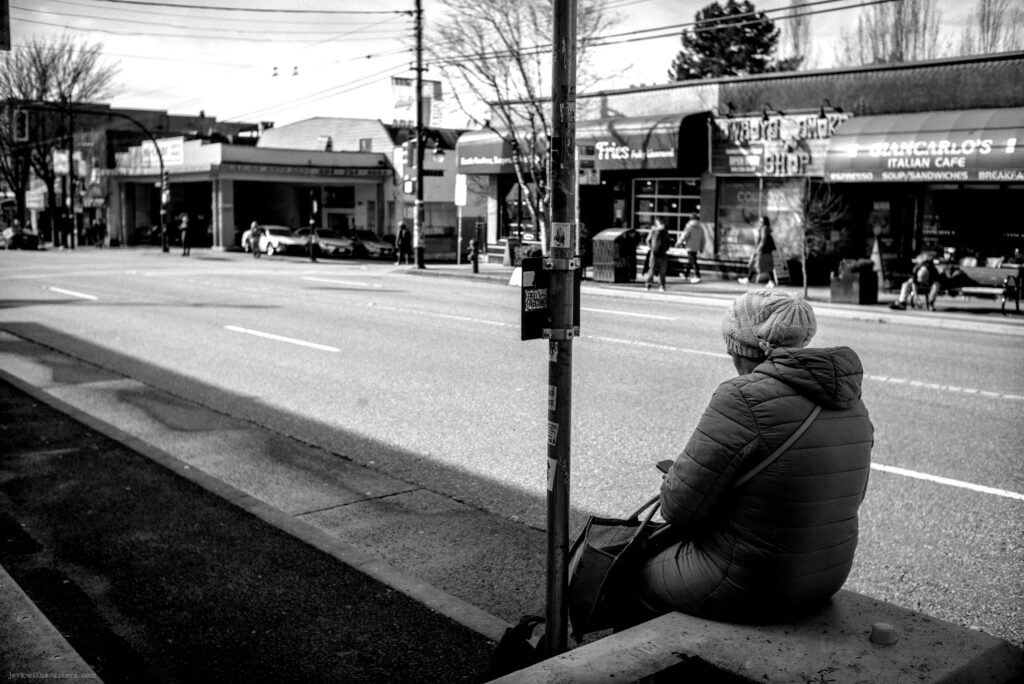 Person sitting at a bus stop looking at phone with traffic in the background