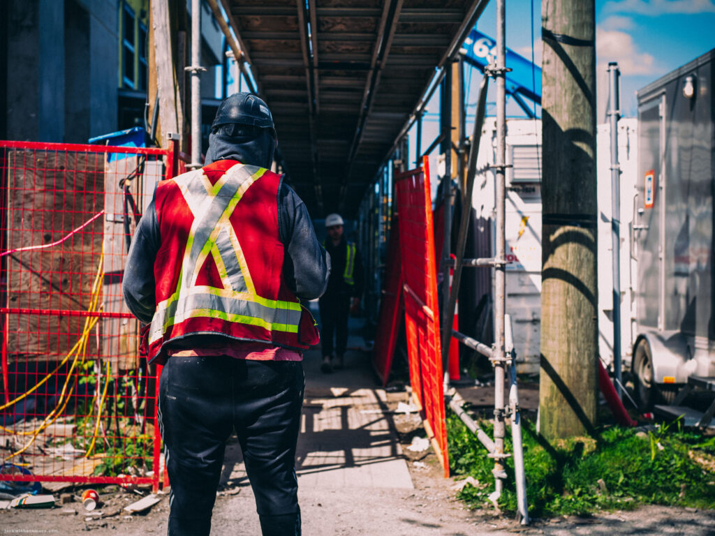 Construction worker in reflective gear standing outside a work site tunnel.