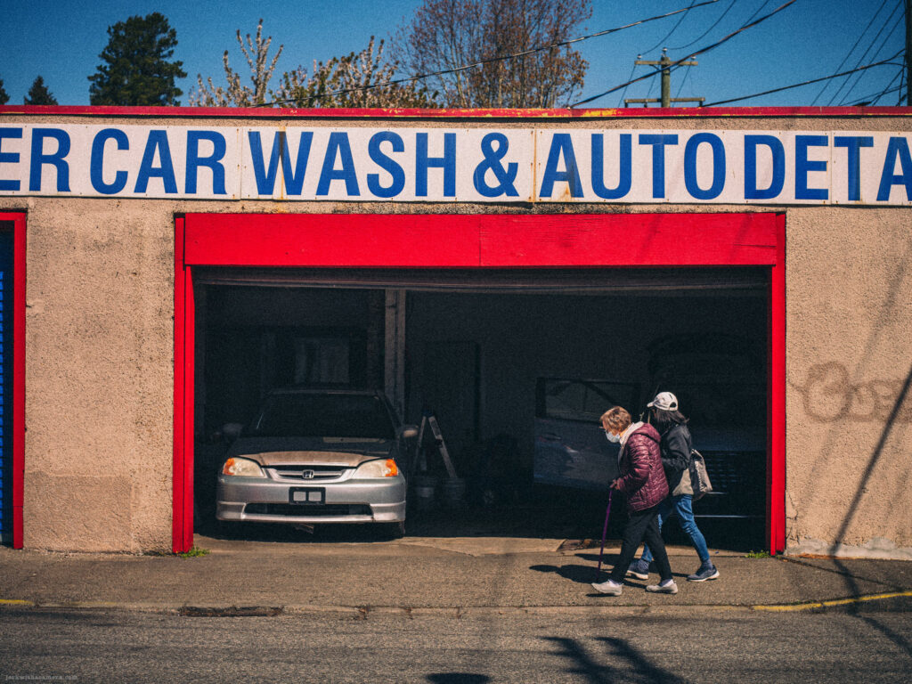 Two people walking past an open garage at a car wash and auto detail shop.