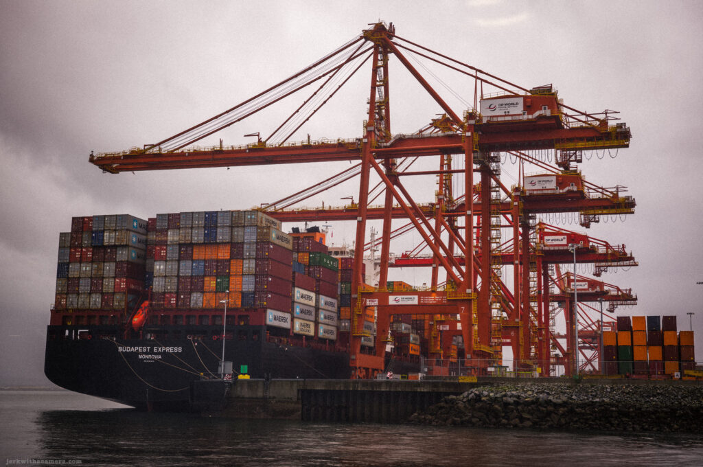 A cargo ship named Budapest Express is docked at a terminal with red cranes and stacked shipping containers.