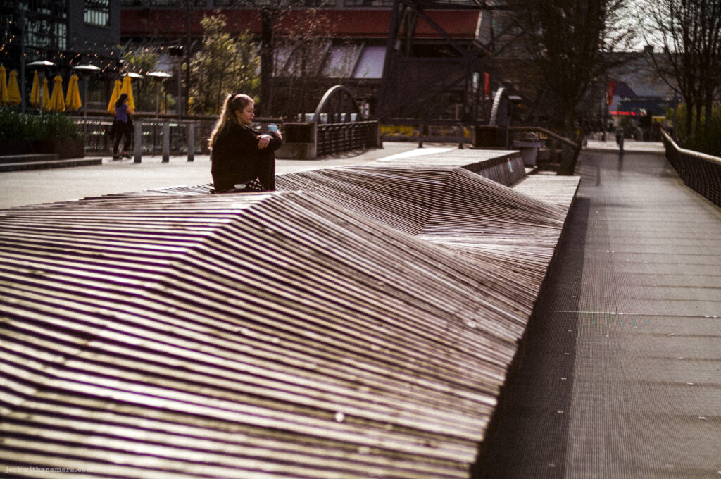 Person sitting on wooden slats in an urban plaza captured with a Leica M-D Typ 262 and the Light Lens Lab 50mm f/1.2 ASPH "1966” lens