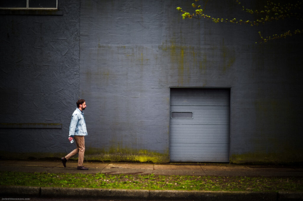 Man walking in front of a grey industrial building with a small garage door.