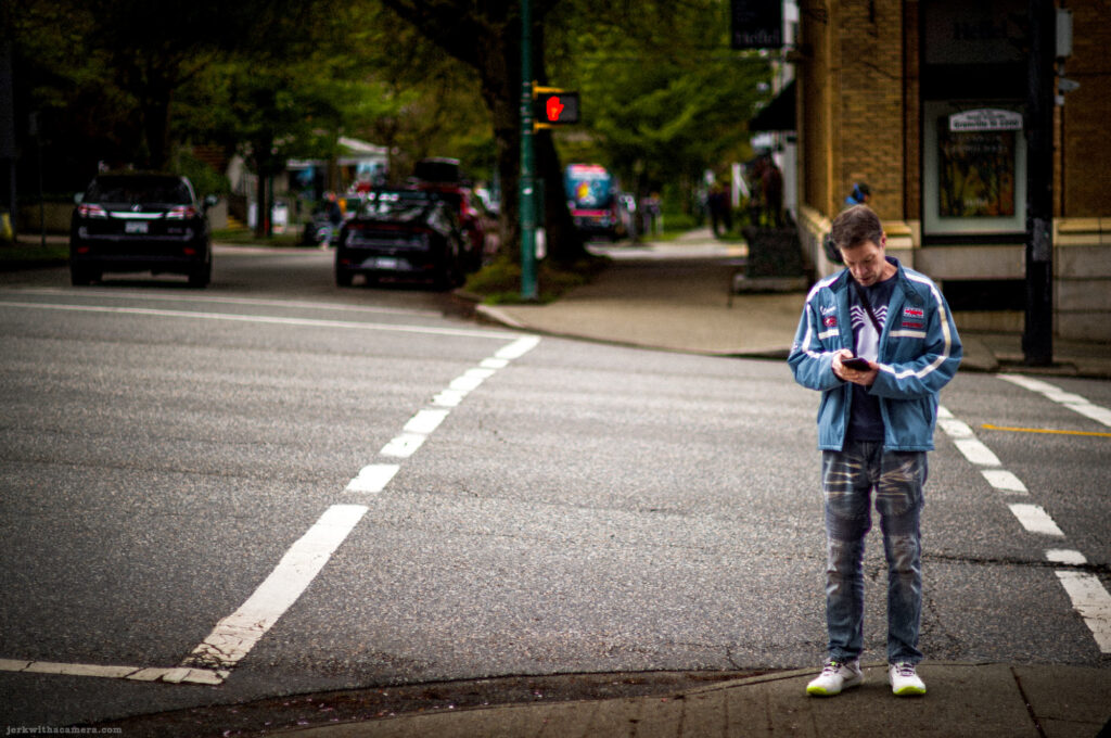 Man looking at his phone while standing at a street corner crosswalk.