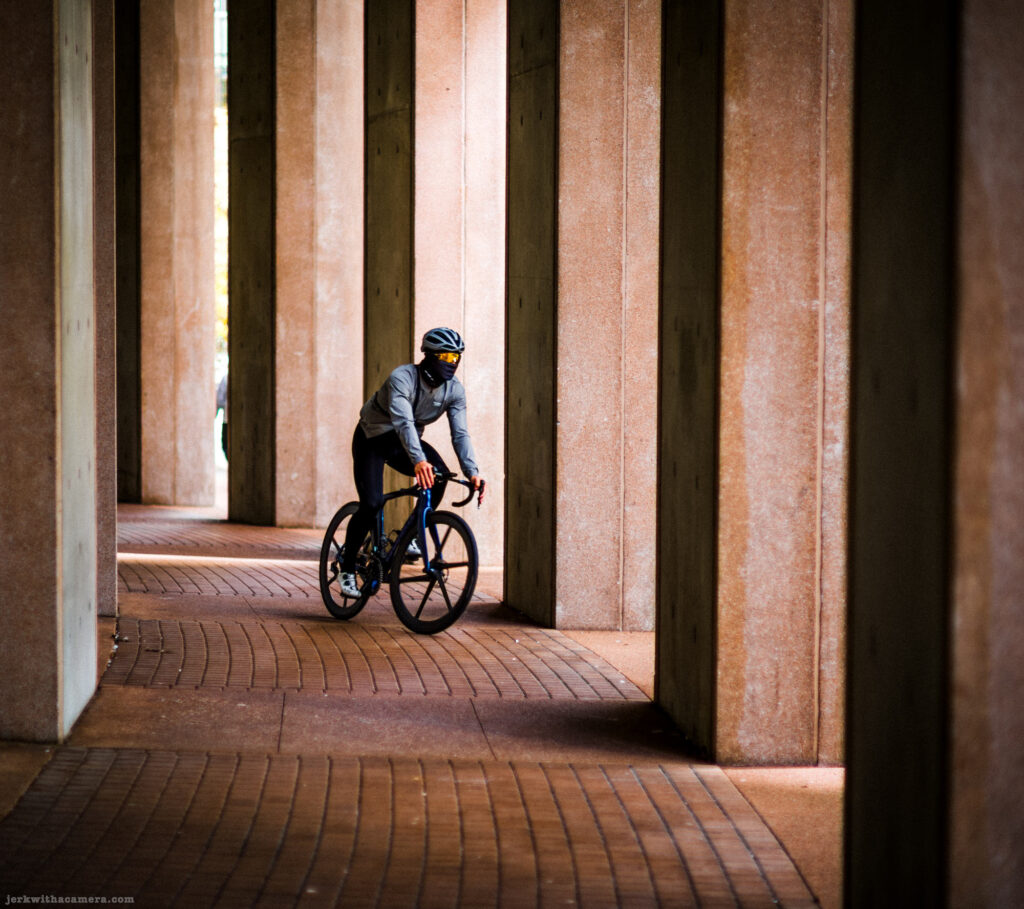Cyclist riding through a corridor of large concrete columns.