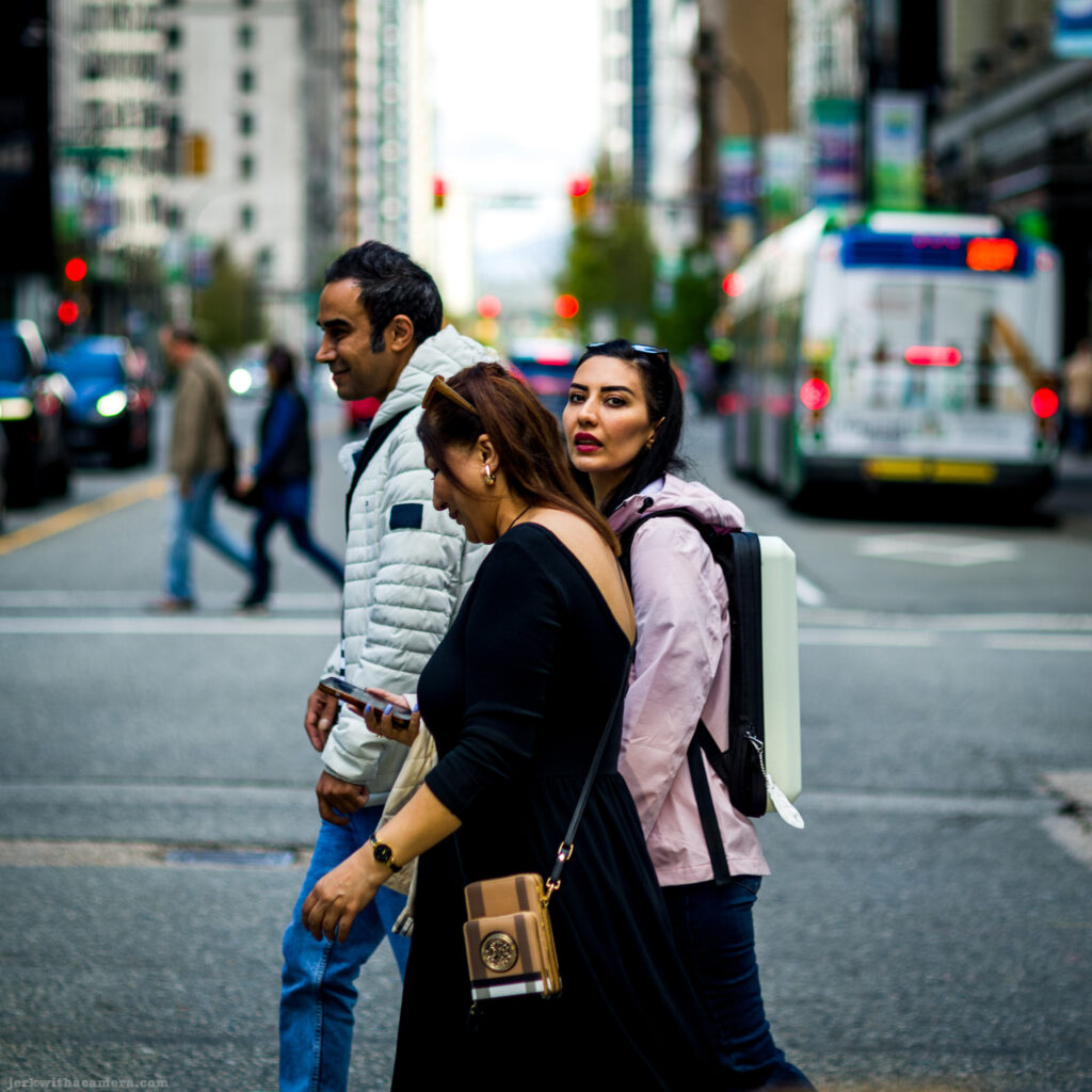 Group of people crossing a city street with traffic and buses in the background.