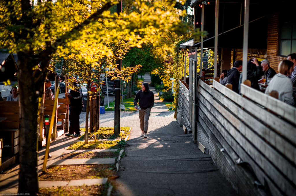 Person walking up a sidewalk beside a restaurant patio during golden hour
